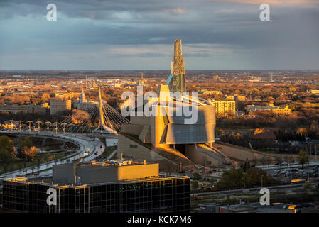 Vue sur le musée pour les droits de l'homme, pont piétonnier de l'Esplanade Riel, avec le Pont Provencher à travers une fenêtre d'hôtel au coucher du soleil le centre-ville de Winnipeg au Manitoba, Canada. Banque D'Images