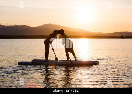 Un jeune couple en silhouette se prépare à embrasser tout en pédarant dans Comox Bay. La vallée de Comox, île de Vancouver, Colombie-Britannique, Canada. Banque D'Images