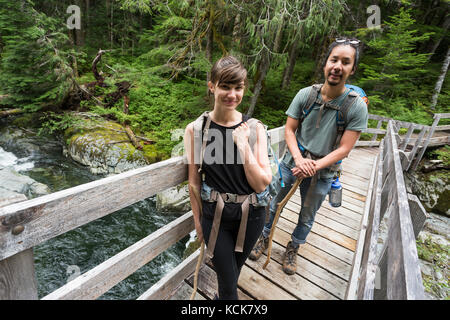 Un jeune couple de randonnée Lac bedwell traverse une passerelle près de la fin de la piste, parc Strathcona, centre de l'île de Vancouver, Colombie-Britannique, Canada Banque D'Images