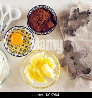 Ingrédients pour la cuisson sur une table de marbre blanc : farine, œufs, poudre de cacao, sucre, beurre et cuillères à mesurer, moules Banque D'Images