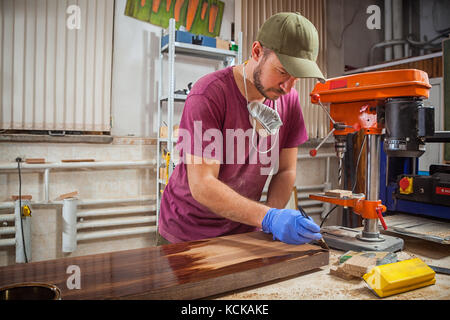 Un homme en chemise de travail et marchandise verte en bois peint une brosse avec une brosse en bois pour la protection contre la corrosion dans l'atelier, dans le background Banque D'Images