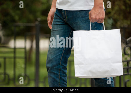 L'homme avec un sac en papier blanc dans les mains sur un arrière-plan Parc. courier avec un sac sur l'arrière-plan d'un parc verdoyant Banque D'Images