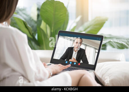 Jeune femme assise sur un canapé communique avec l'homme en costume officiel via l'application d'appels vidéo. couple chatting. relation à distance, les pers Banque D'Images