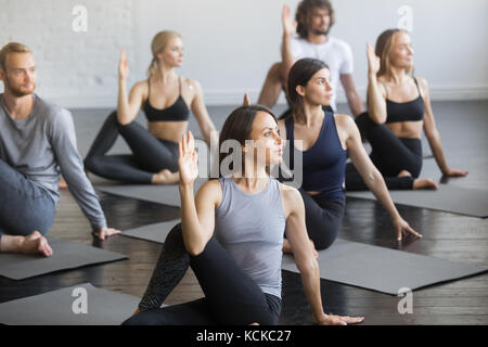 Groupe de jeunes sportifs pratiquant le yoga leçon avec instructeur, assis dans la moitié seigneur des poissons l'exercice, ardha matsyendrasana posture, groupe de travail o Banque D'Images