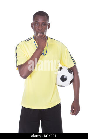 Arbitre de football tenant une balle avec un sifflet dans sa bouche Banque D'Images