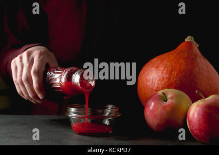 Bouteille avec canneberge dans la main, la citrouille et les pommes sur la table horizontale Banque D'Images