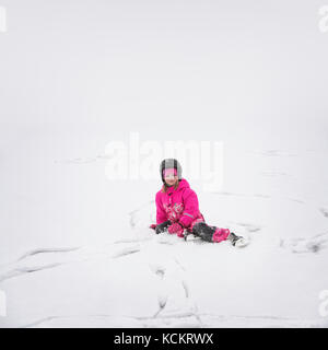 Jeune fille avec casque de patinage sur glace assis dans la neige sur la glace après une chute Banque D'Images