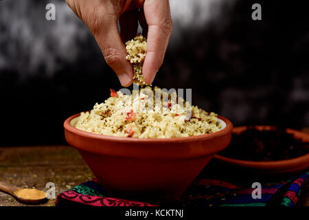 Libre d'un jeune homme obtenir certains taboulé, une salade arabe levantin typique, avec sa main d'un bol en terre cuite placé sur un set de table pour le déjeuner Banque D'Images