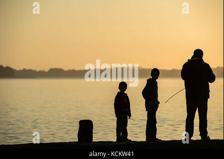 Silhouette d'un homme et ses deux enfants avec des cannes à pêche, dans le golfe du Morbihan, dans la soirée, à Vannes (Bretagne, nord-ouest de la France). Le Banque D'Images