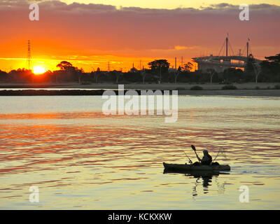 Pêche en canoë au coucher du soleil avec Port Melbourne au-delà et silhouette du pont Westgate à droite. Melbourne, Victoria, Australie Banque D'Images