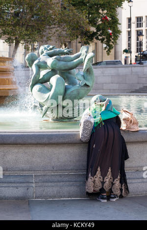 Femme en robe traditionnelle Asiatique, à la recherche dans une fontaine à Trafalgar Square, London, England, UK Banque D'Images