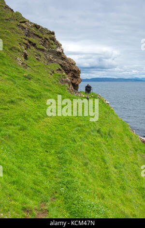 Une marchette sur la piste sous les falaises du côté ouest du plateau Beinn Bhuidhe, île d'Eigg, Écosse, Royaume-Uni Banque D'Images