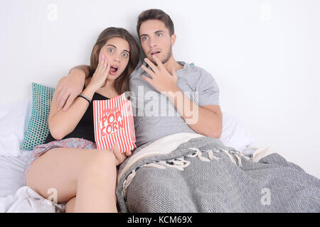 Jeune couple à regarder des films au lit et eating popcorn. à l'intérieur. Banque D'Images