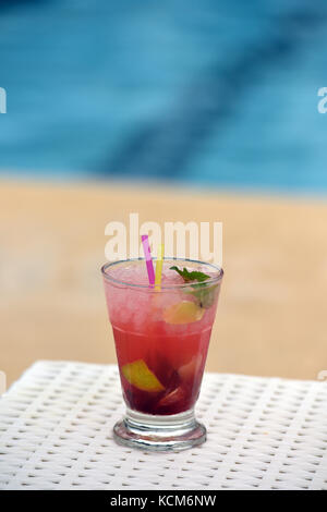 Un cocktail coloré avec paille et parapluie à côté d'une piscine prête à boire. Banque D'Images