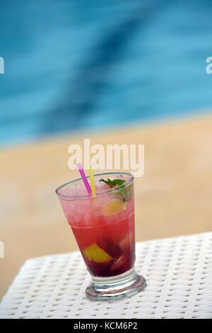 Un cocktail coloré avec paille et parapluie à côté d'une piscine prête à boire. Banque D'Images