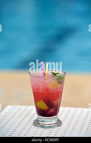 Un cocktail coloré avec paille et parapluie à côté d'une piscine prête à boire. Banque D'Images