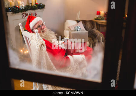 Portrait du père noël assis avec pile de boîtes-cadeaux dans la salle de séjour pendant la période de Noël Banque D'Images