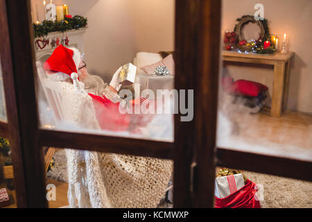 Le père Noël à la recherche de coffrets cadeaux dans la salle de séjour à la maison pendant la période de Noël Banque D'Images