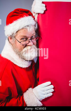 Père Noël peeking de planche rouge contre fond blanc Banque D'Images