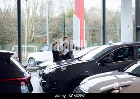 Vendeur avec female customer holding tout en se tenant dans le document car showroom Banque D'Images