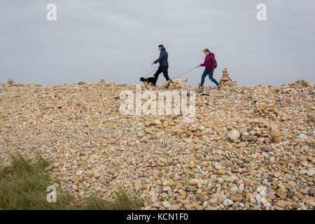 Un couple de propriétaires de chiens soigneusement choisir leur chemin sur les roches et les pierres sur l'Île Sainte, le 27 septembre 2017, sur l'île de Lindisfarne, Northumberland, Angleterre. L'île sacrée de Lindisfarne, également connu simplement comme Holy Island, est une île au large de la côte nord-est de l'Angleterre. Holy Island a une histoire enregistrée à partir de la 6ème ANNONCE de siècle ; il a été un centre important de l'Anglo-saxon, celte et le christianisme. Après les invasions vikings et la conquête normande de l'Angleterre, un prieuré a été rétablie. Banque D'Images