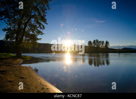 Le soleil du soir se couche derrière les montagnes qui entourent la rivière Shuswap à Enderby dans la région de Shuswap de la Colombie-Britannique, Canada Banque D'Images