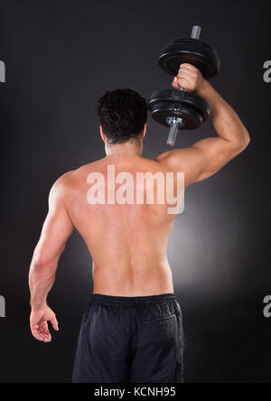 Young man exercising with dumbbells musculaire sur fond noir Banque D'Images