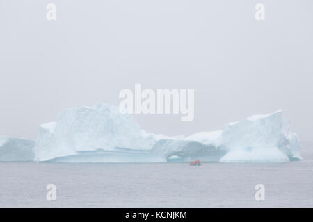 Un éclairage couvert doux illumine un grand iceberg et le zodiak dans le détroit de Gerlache. Péninsule Antarctique Banque D'Images