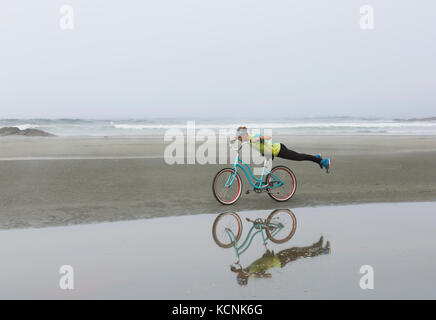 Un cavalier avec un tie dye t-shirt joue sur son beach cruiser alors que sur Chesterman Beach. Tofino, Vancouver Island, British Columbia, Canada. Banque D'Images