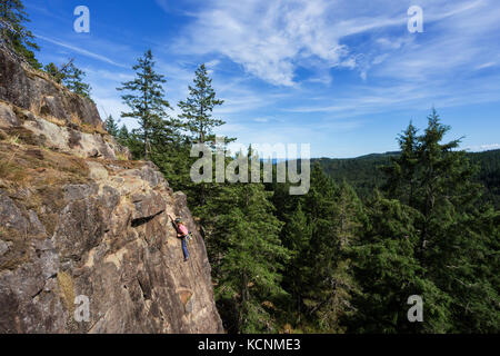 Une femme grimpeur de roche monte sur un itinéraire sur l'une des zones d'escalade près de la montagne chinoise. Quadra Island. Banque D'Images