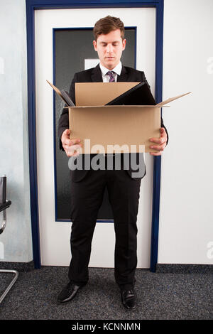 Portrait of young businessman holding cardboard in office Banque D'Images