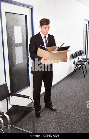 Portrait of young businessman holding cardboard in office Banque D'Images