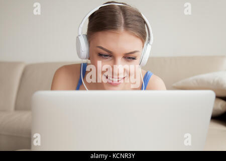 Smiling young woman wearing headphones using laptop, teen girl faisant appel vidéo, regarder, étudier en ligne à la maison, à l'écoute de cours audio, Banque D'Images