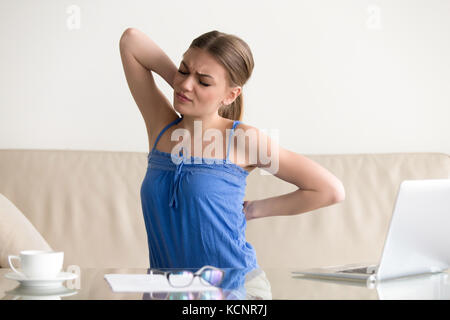 Young woman stretching souffrant de maux de dos, soudain tendu muscles après de long travail sédentaire dans les mauvaises postures à la maison, a souligné girl ba Banque D'Images