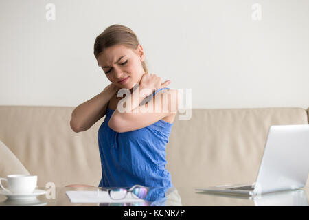 Sentiment femme fatiguée d'une douleur au cou, masser les muscles tendus, souffrant de maux de dos épaule chronique après un long travail sur l'ordinateur portable à la maison, sedentar Banque D'Images