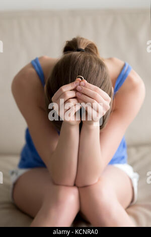 Contrarié young woman holding anneau de mariage assis sur sa tête en bas de la table, trahi femme pleurer sur le mariage ruine, triché girl enfoncé après breaki Banque D'Images