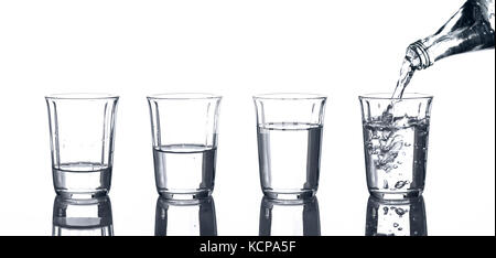 4 verres à l'eau et une bouteille de ce qui est versée. Banque D'Images