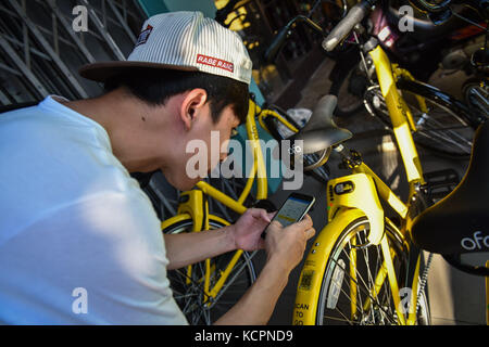 Phuket, Thaïlande. 5 octobre 2017. Un touriste est sur le point de débloquer un vélo de partage ofo dans une zone commerciale de Phuket, Thaïlande, Oct. 5, 2017. La société chinoise de partage de vélos sans quai ofo a fourni plus de 1 000 vélos dans les endroits clés de Phuket fin septembre et a offert un essai gratuit d'un mois sans frais de dépôt. Maintenant, le service de partage de vélos a profité aux résidents locaux et aux touristes. Les frais de service réguliers d'OFO seront facturés à 5 Baht par 30 minutes d'utilisation, avec des frais de dépôt de 99 Baht. Crédit : Li Mangmang/Xinhua/Alamy Live News Banque D'Images