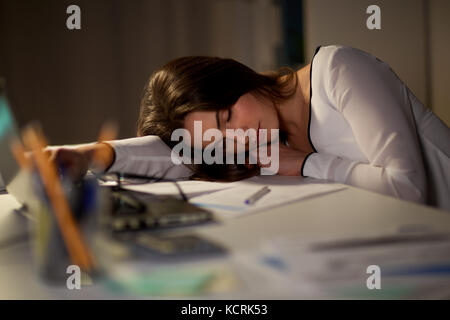 Tired woman sleeping on table office de nuit Banque D'Images