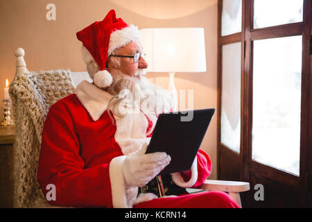 Thoughtful santa claus using digital tablet in living room pendant la période de Noël Banque D'Images