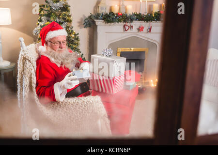 Le père Noël à la recherche de coffrets cadeaux dans la salle de séjour à la maison pendant la période de Noël Banque D'Images