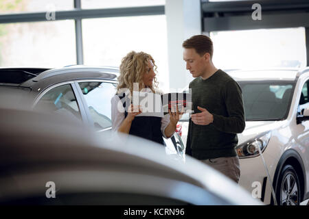 Saleswoman holding brochure en position debout avec le client dans la salle d'exposition de voiture Banque D'Images