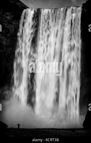 Homme se tenait en face de cascade Skogafoss montrant la taille et l'échelle de la cascade dans Skoga, Islande Banque D'Images