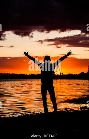 Silhouette de l'homme levant les mains ou bras ouverts quand le soleil se levant. Banque D'Images