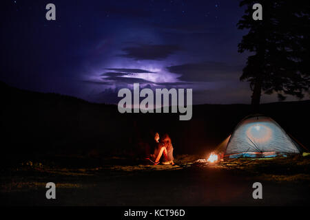 Nuit en camping dans les montagnes. Couple de touristes ont un reste à un feu allumé sous la tente près de l'incroyable nuit ciel plein d'étoiles et Milky Way. l Banque D'Images