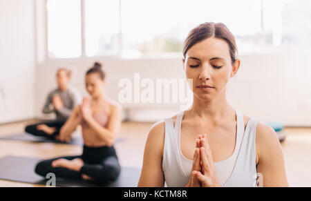 Femme en bonne santé faisant du yoga dans les cours d'éducation physique avec les gens en arrière-plan. Personnes méditant au club de santé. Banque D'Images