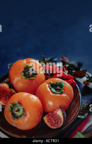 La vie encore automne sombre, les kakis mûrs sur une plaque de bois avec les feuilles d'automne. Fruits de saison close-up. dark la photographie culinaire avec copie espace. Banque D'Images