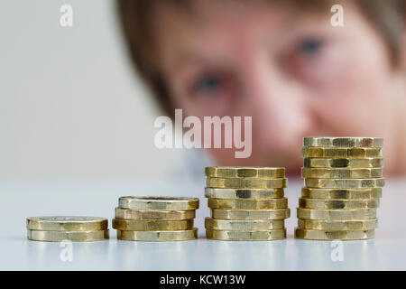 Un pensionné à préoccupé par une pile de livres sterling l'argent britannique de nouvelles pièces livre GBP en quatre piles. Watch épargne placements concept UK Banque D'Images