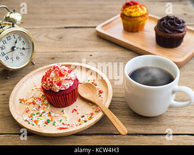 Cupcakes rouges mis sur une plaque en bois à côté de sphérique a cupcake Vintage réveil et tasse à café blanc à l'arrière-plan sont jaunes et cupcake Banque D'Images
