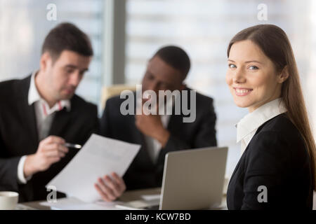 Portrait de jeune femme en costume formel assis sur la négociation d'affaires, réunion ou entretien avec african american and Caucasian businessmen re Banque D'Images